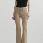 A model wearing beige flared jeans and a black sleeveless top, standing against a light gray studio background.