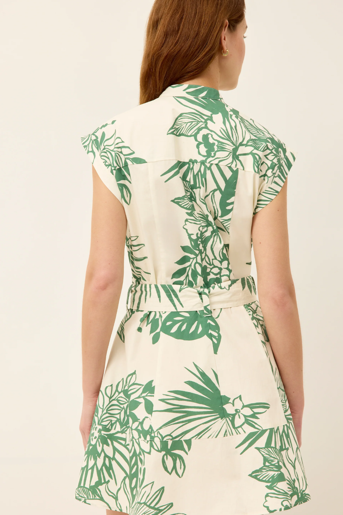 Woman wearing a white dress with green leaf pattern on a plain background