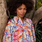 Woman wearing a colorful patterned shirt standing against a natural background