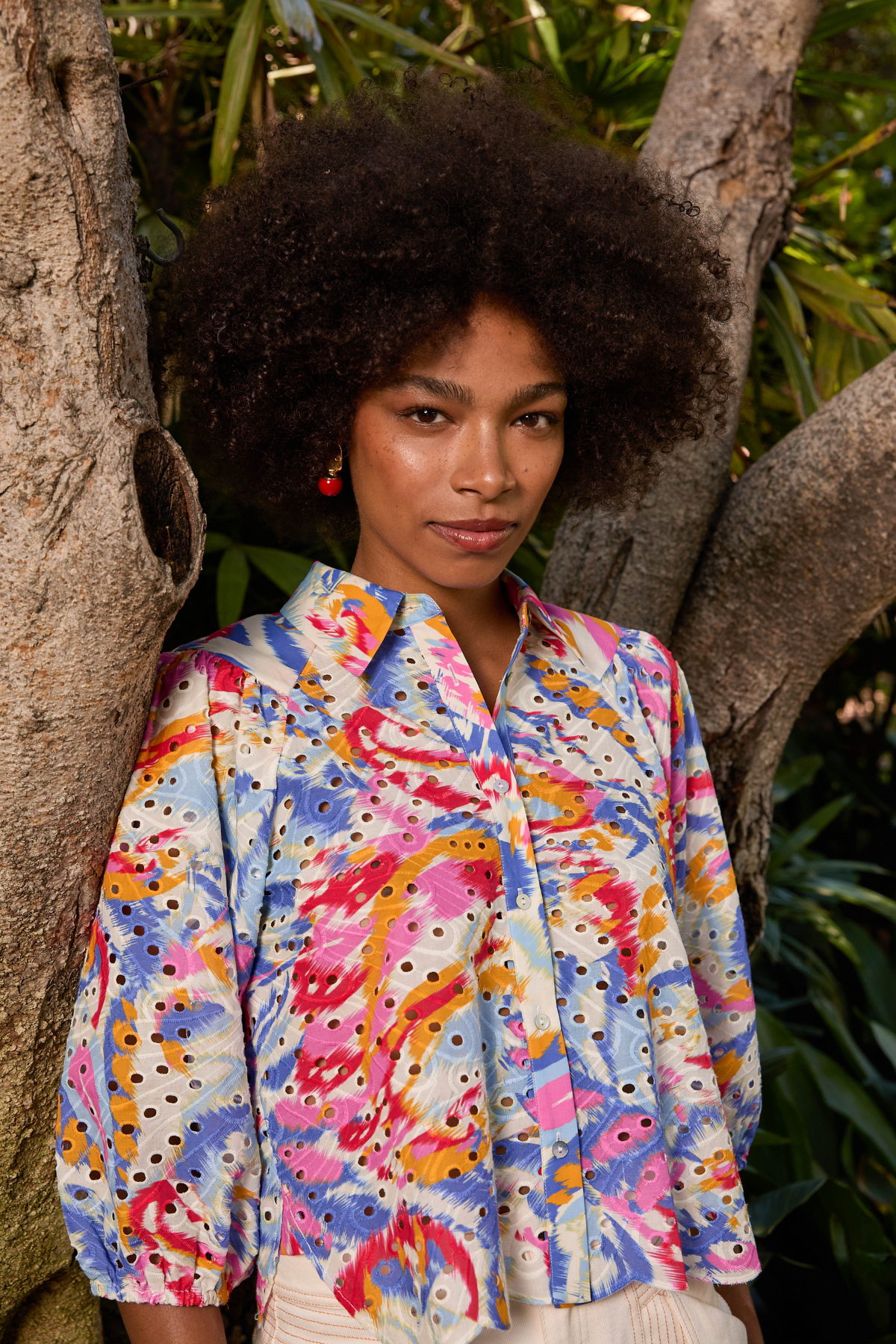 Woman wearing a colorful patterned shirt standing against a natural background