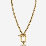 A gold-toned chain necklace featuring a large toggle clasp and a circular medallion pendant with a sunburst or floral pattern, shown against a plain light gray background.