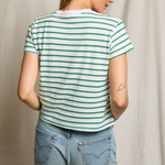 Person wearing a green and white striped t-shirt and blue jeans against a neutral background