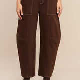 A model is shown from the waist down wearing dark brown wide-leg cropped pants with a matching dark brown belt featuring a gold buckle, paired with dark brown ankle boots against a solid beige background.
