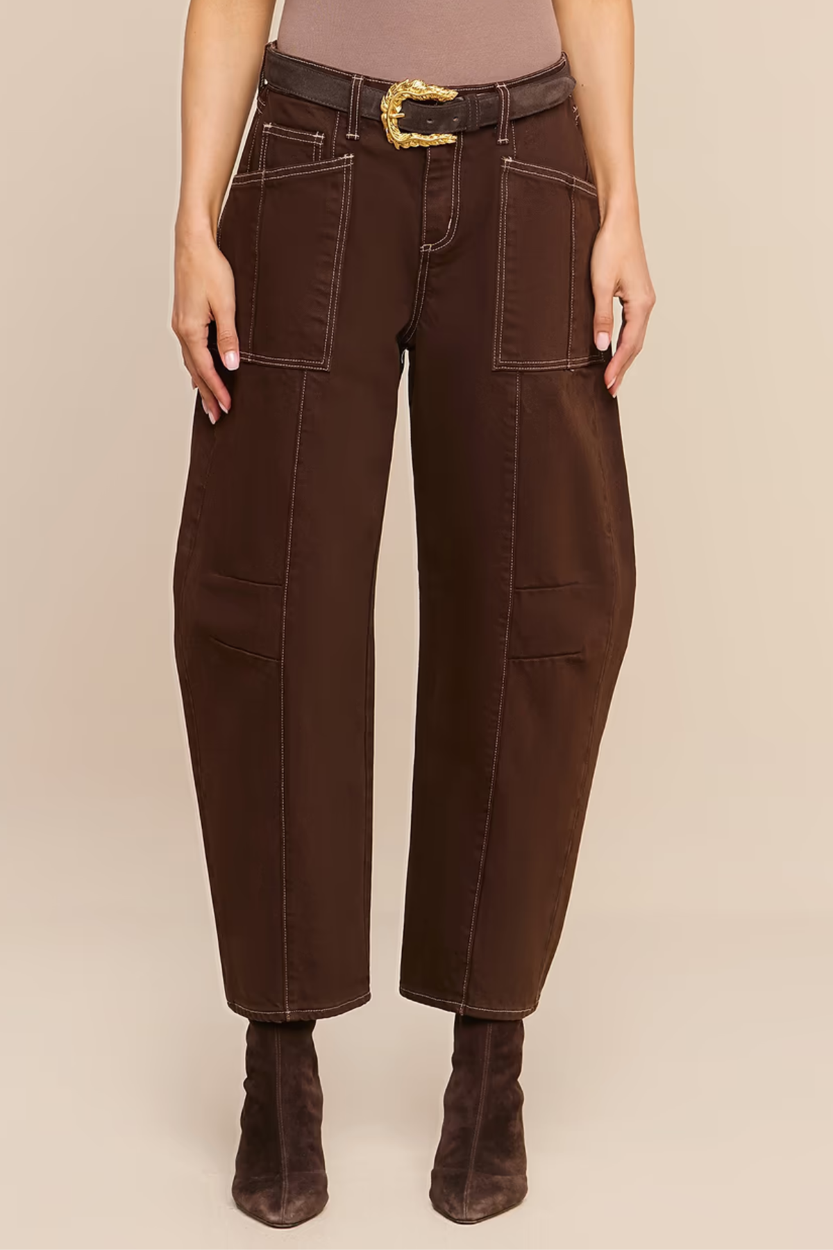 A model is shown from the waist down wearing dark brown wide-leg cropped pants with a matching dark brown belt featuring a gold buckle, paired with dark brown ankle boots against a solid beige background.