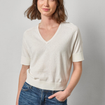 Woman wearing a white sweater and blue jeans against a gray background