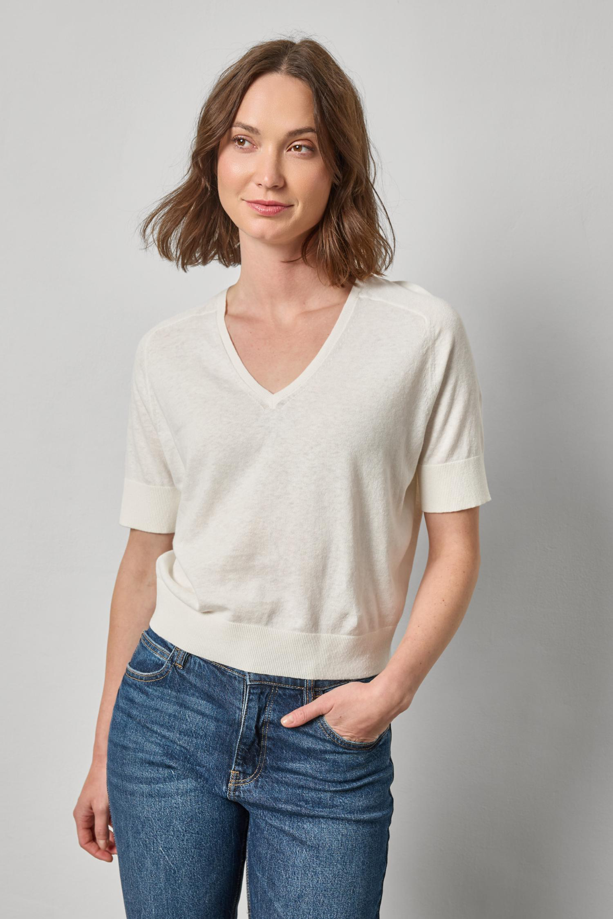 Woman wearing a white sweater and blue jeans against a gray background