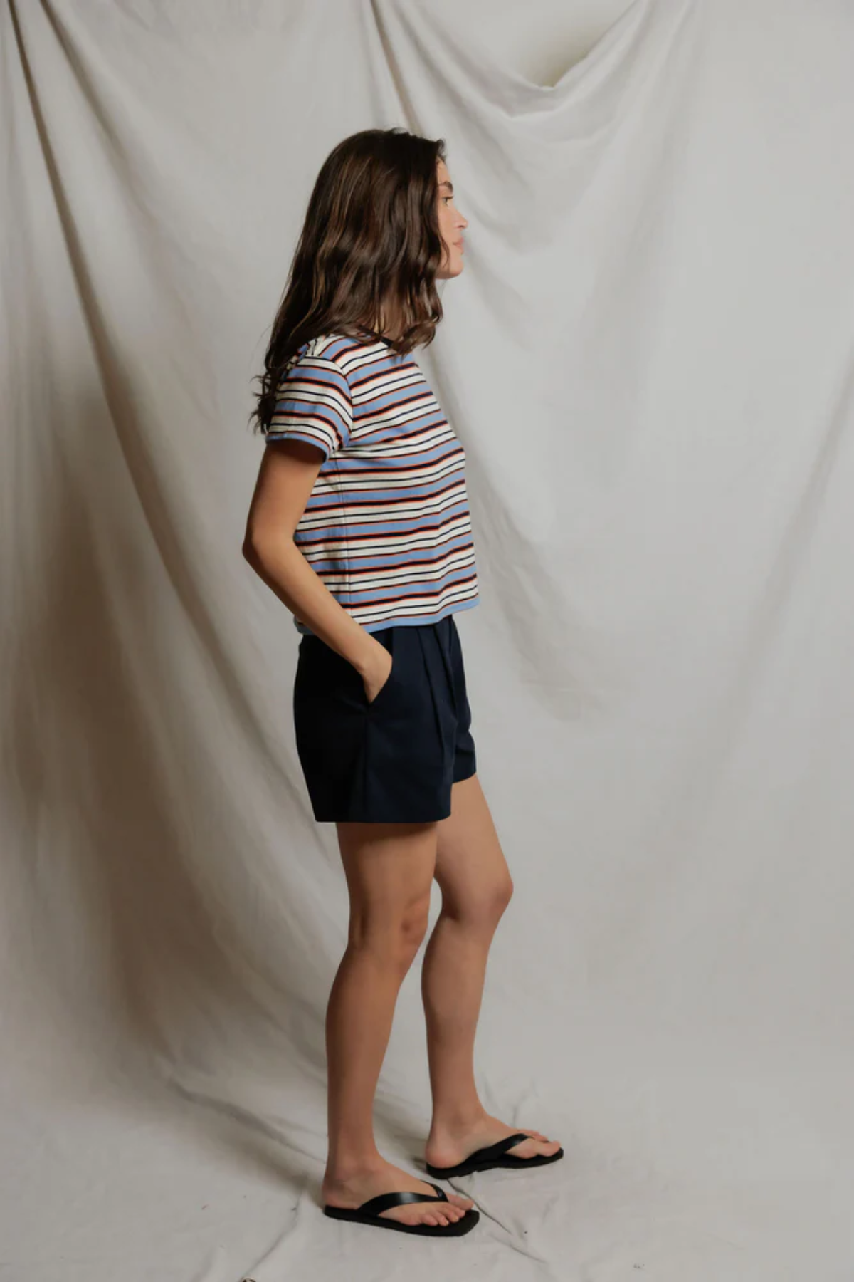 Person wearing a striped shirt and dark shorts against a plain background