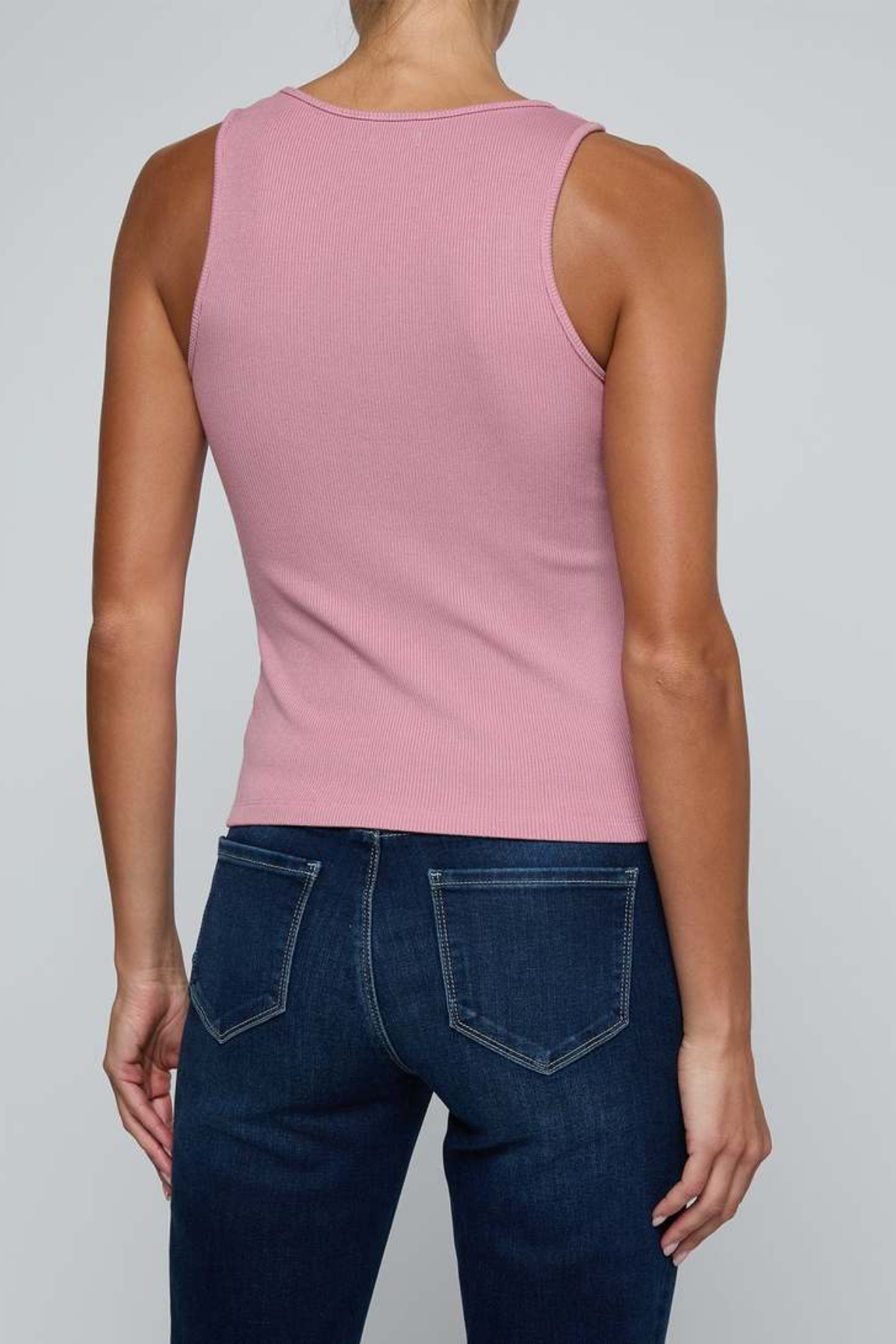 A woman shown from the back wearing a fitted sleeveless pink top and dark blue jeans against a light gray studio background.