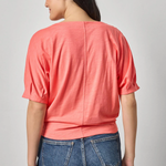 Person wearing a coral top and blue jeans on a plain background