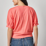 Person wearing a coral top and blue jeans on a plain background