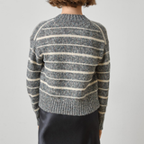 A model viewed from the back wearing a gray and cream striped knit sweater and a dark skirt, set against a plain light gray studio background.