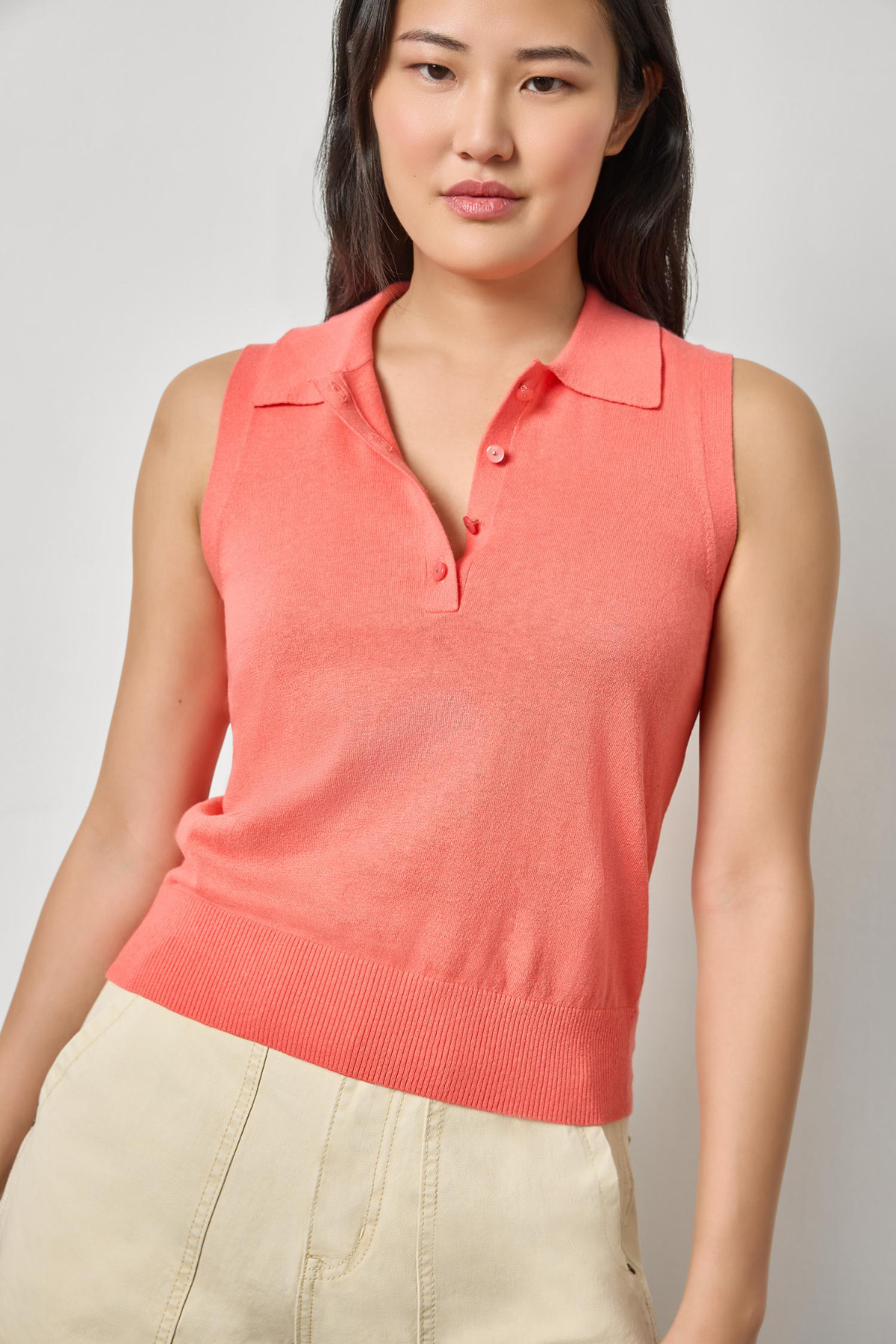 Woman wearing a coral sleeveless polo shirt against a plain background