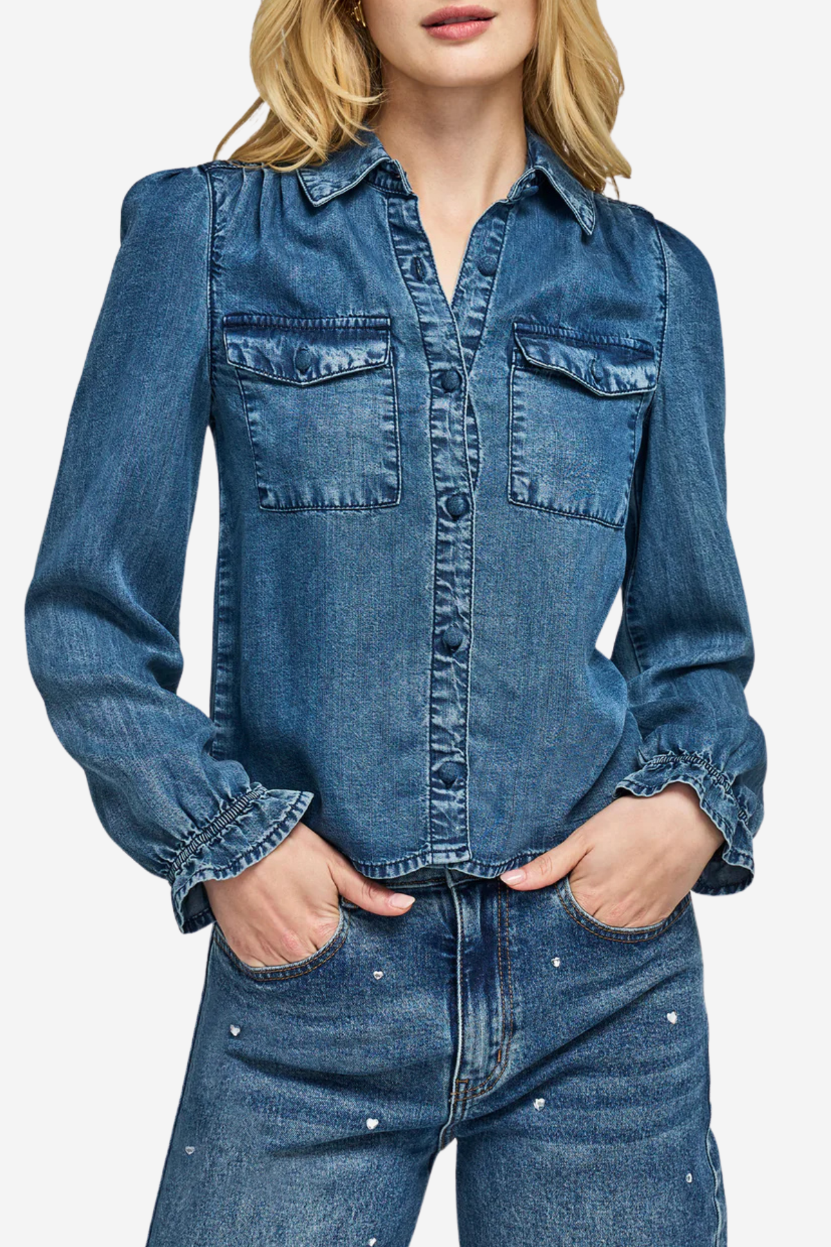 A woman wearing a blue denim long-sleeve button-up shirt with chest flap pockets and matching embellished jeans, shown against a plain light background.