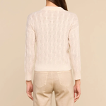 A woman shown from the back wearing a cream-colored textured knit cardigan and beige trousers, set against a solid beige studio background.