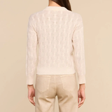 A woman shown from the back wearing a cream-colored textured knit cardigan and beige trousers, set against a solid beige studio background.