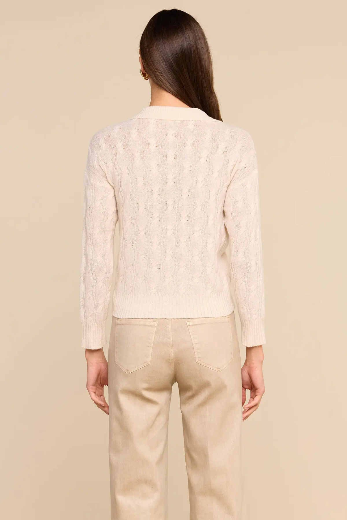 A woman shown from the back wearing a cream-colored textured knit cardigan and beige trousers, set against a solid beige studio background.