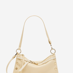 A light beige leather shoulder bag with gold-tone hardware, featuring a crescent-shaped body, a long shoulder strap, and decorative rivet details on the sides, set against a plain white background.