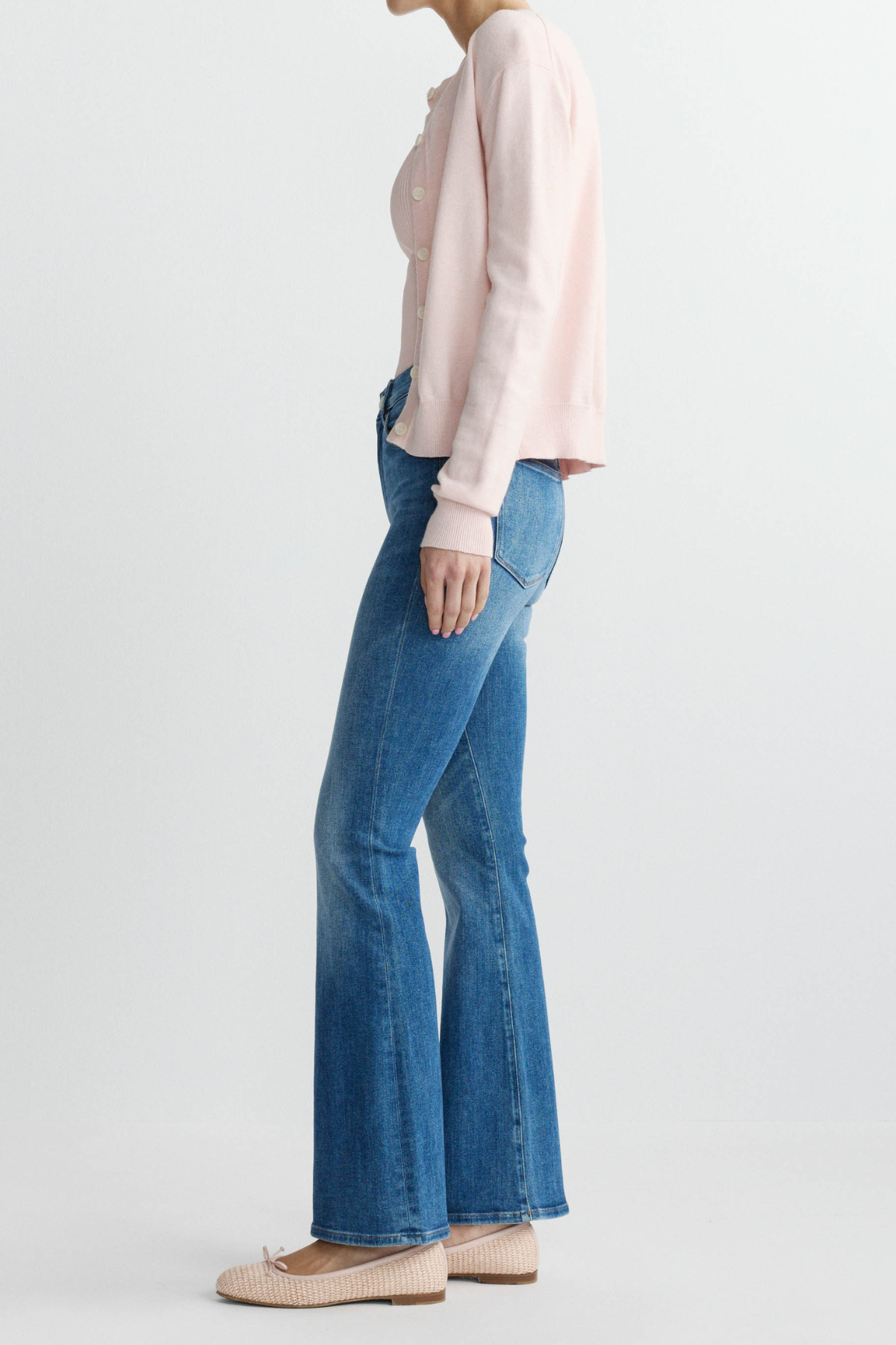 Person wearing a light pink blouse and blue flared jeans on a white background