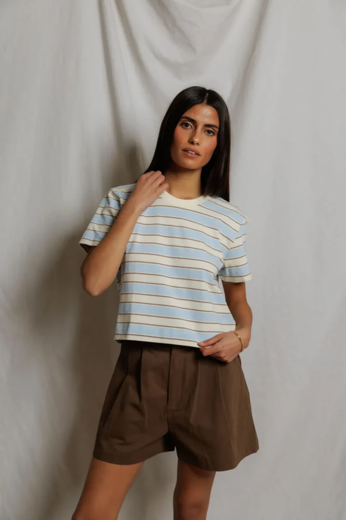 Woman wearing a striped shirt and brown shorts against a plain background