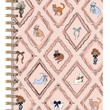 A spiral-bound notebook with a light pink cover featuring a repeating diamond pattern decorated with various illustrated cats in different poses and colors, bound with gold-tone metal coils on the left.