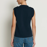 Person wearing a dark blue sleeveless top and blue jeans on a plain background