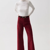 A woman modeling a white mock-neck long-sleeve top and burgundy wide-leg cropped trousers with a black belt, paired with black pointed-toe heels, against a light gray studio background.