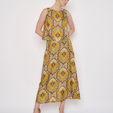A woman modeling a sleeveless midi dress with a yellow, gold, and brown floral pattern, standing against a plain white studio background.