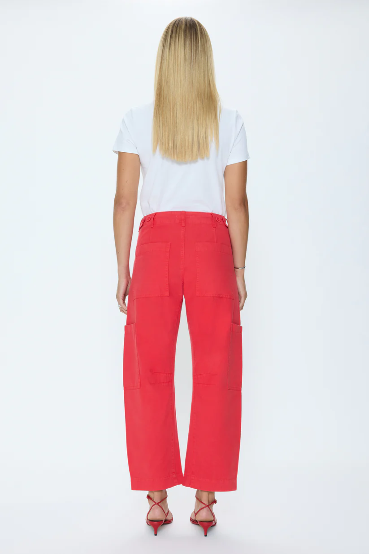 A woman viewed from the back wearing bright red wide-leg cropped pants, a white short-sleeve T-shirt, and red strappy heels against a plain white studio background.