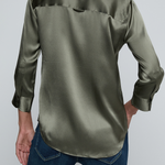 Model wearing dark green blouse with jeans on off white background.