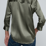 Model wearing dark green blouse with jeans on off white background.
