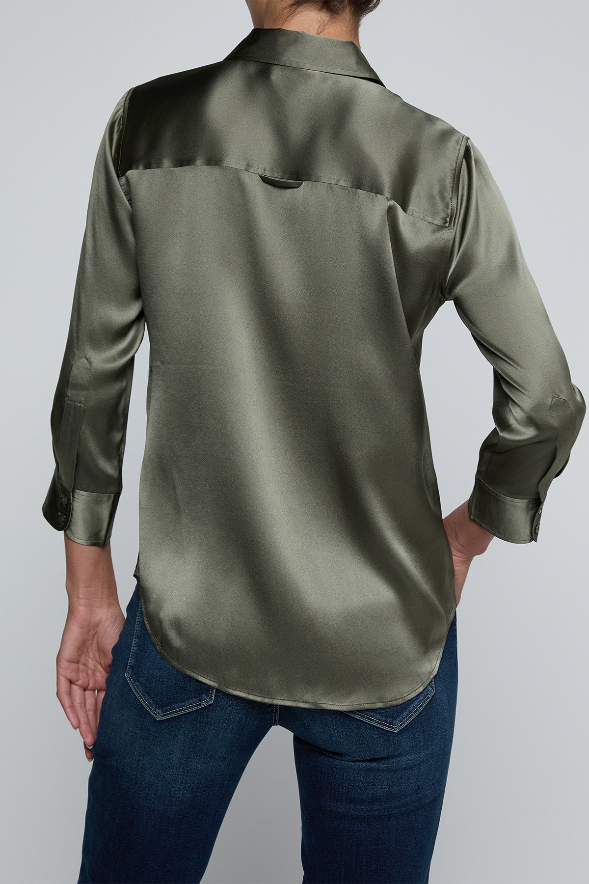 Model wearing dark green blouse with jeans on off white background.