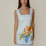 Woman wearing a sleeveless dress with floral and fruit design on a plain background