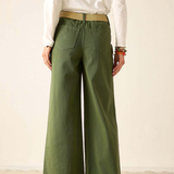 A person shown from the back wearing olive green wide-leg pants with a tan belt, a white long-sleeve top, and brown sandals against a plain cream studio background.