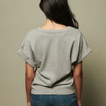 Person wearing a gray oversized t-shirt and blue jeans against a beige background
