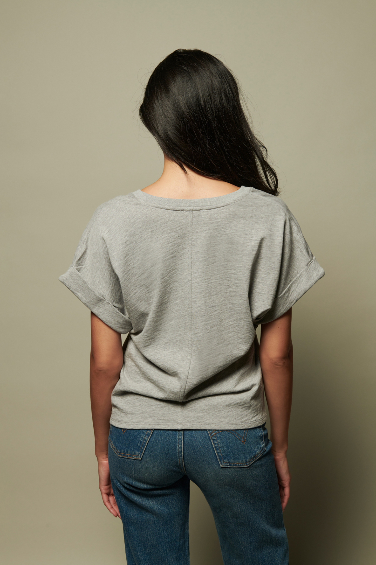 Person wearing a gray oversized t-shirt and blue jeans against a beige background