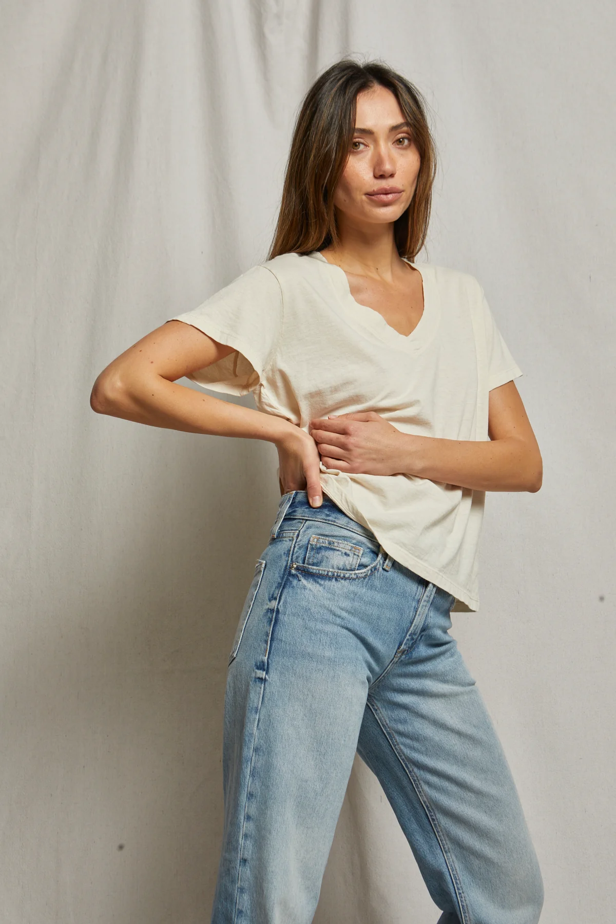 Woman wearing a white top and light blue jeans against a plain background