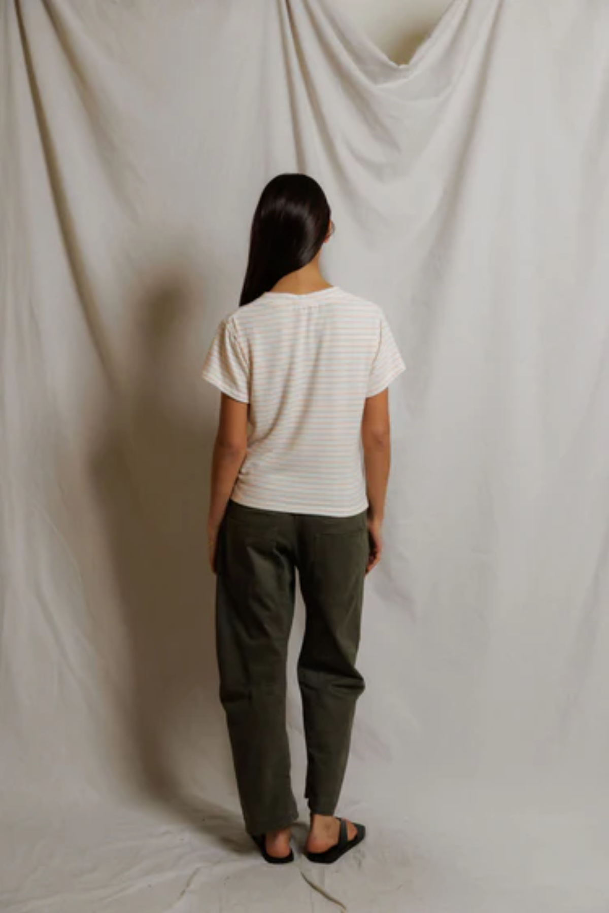Person wearing a white striped shirt and green pants standing against a plain white background