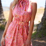 Woman wearing a pink floral dress on a beach with palm trees in the background