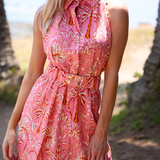 Woman wearing a pink floral dress on a beach with palm trees in the background