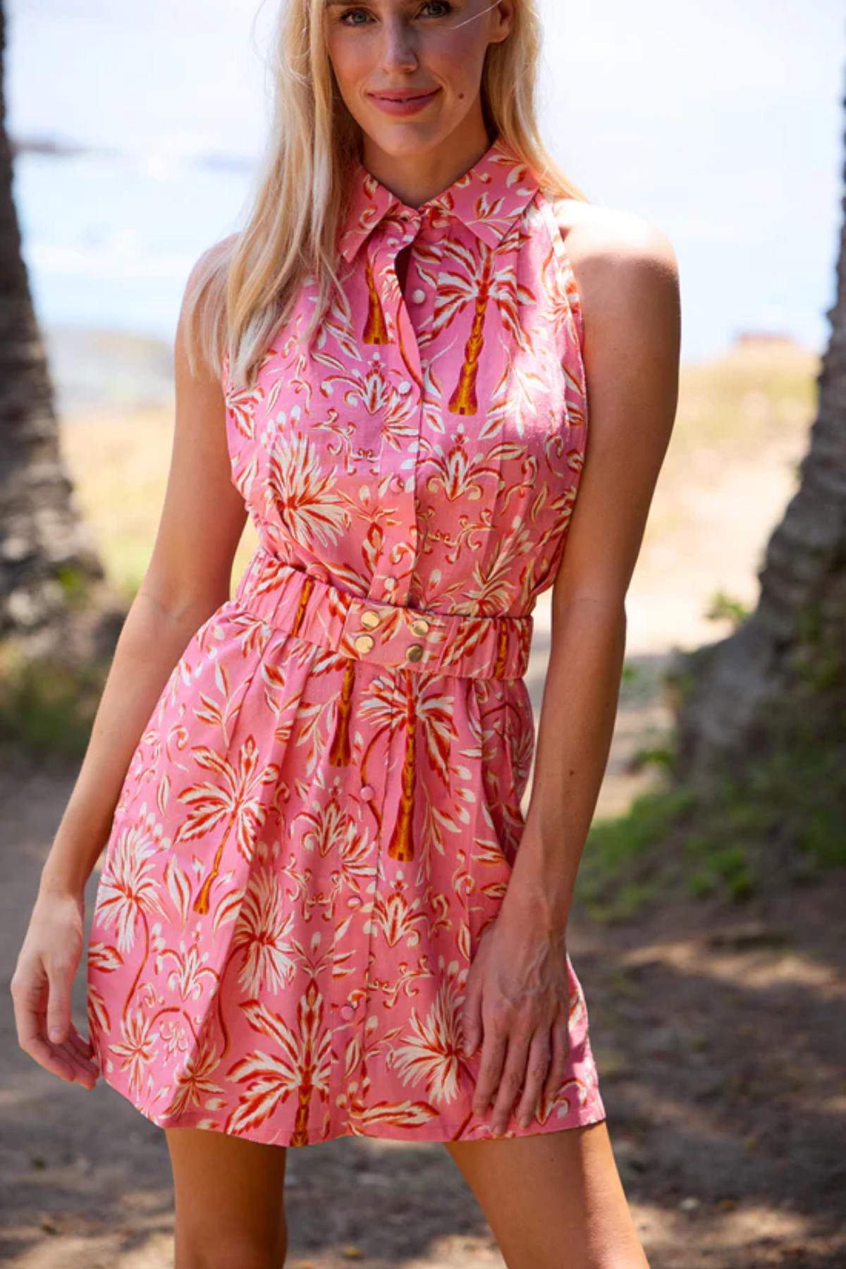 Woman wearing a pink floral dress on a beach with palm trees in the background