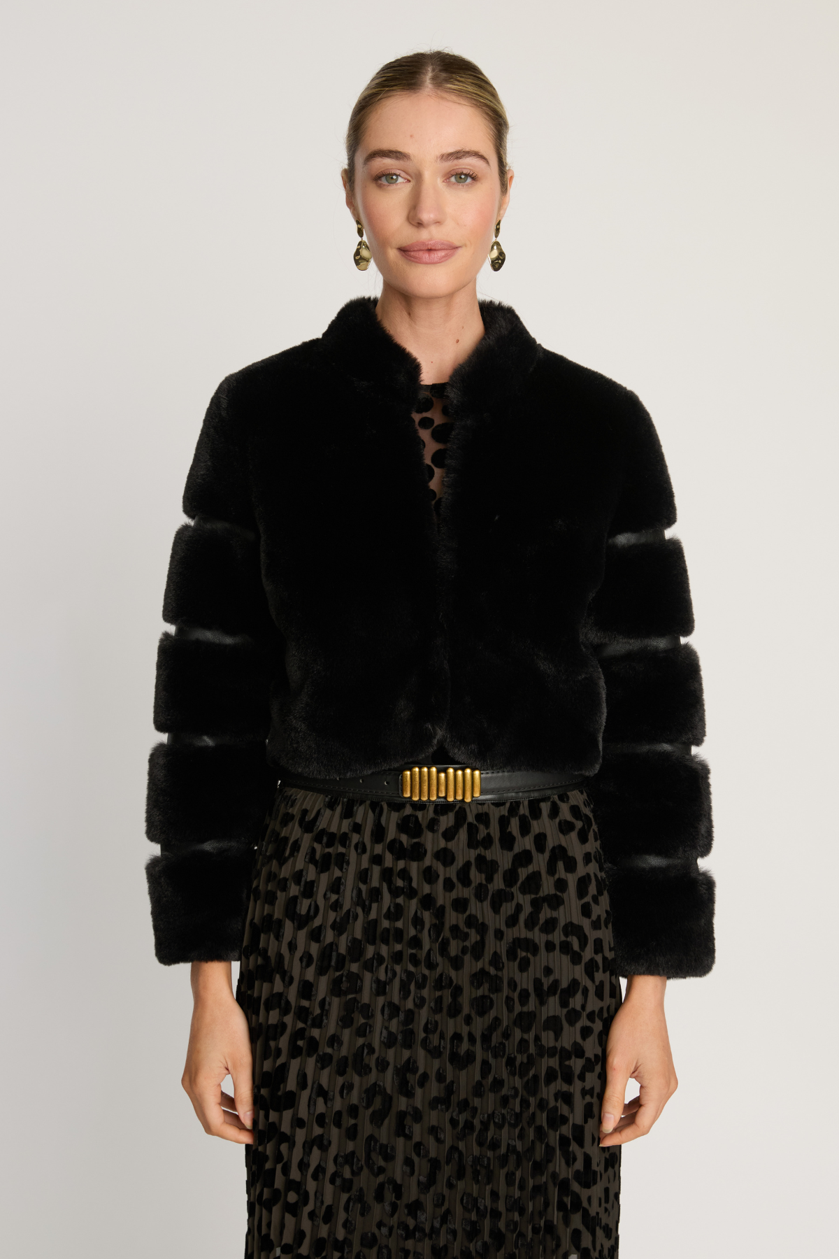 Woman wearing a black fur coat with a gold belt and leopard print skirt on a white background