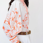 Woman wearing a white blouse with orange floral patterns on a plain background