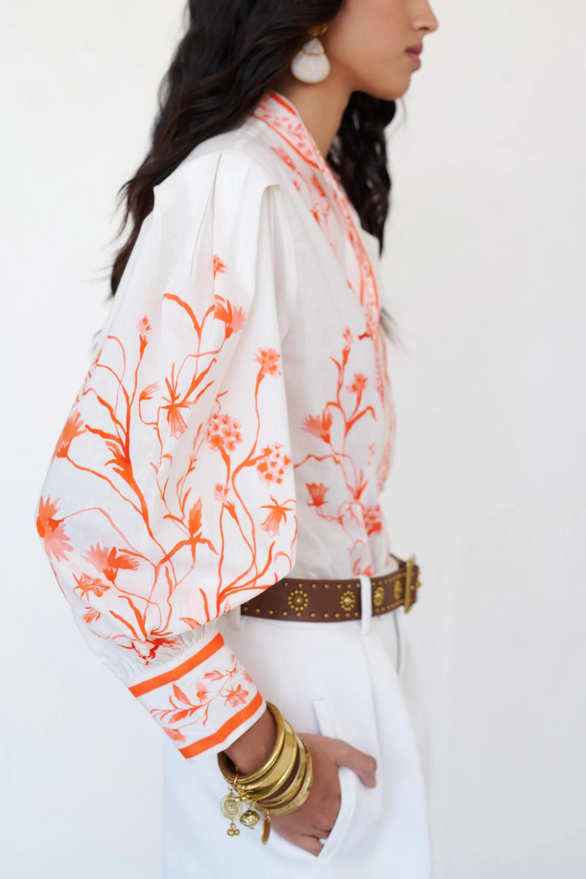 Woman wearing a white blouse with orange floral patterns on a plain background