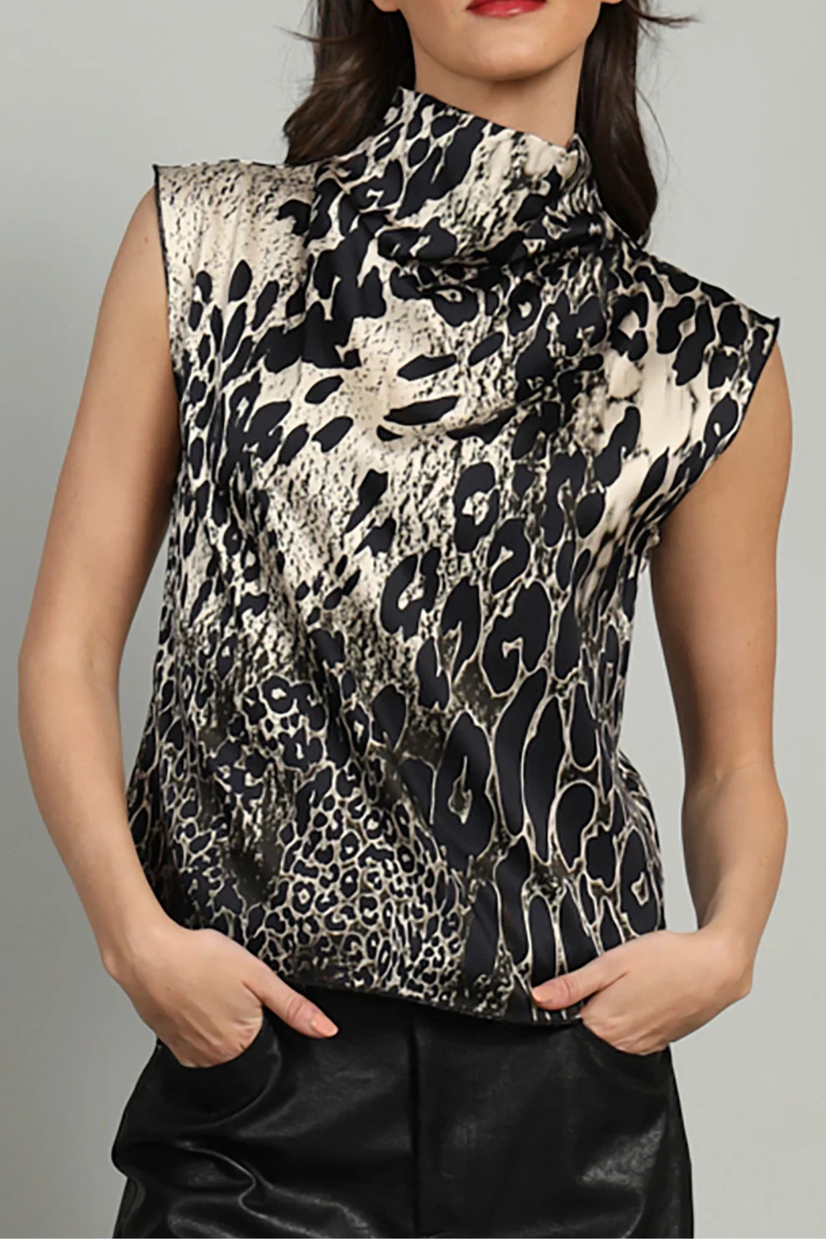 A woman wearing a sleeveless high-neck top with a black and beige animal print pattern, paired with black pants, against a plain gray background.