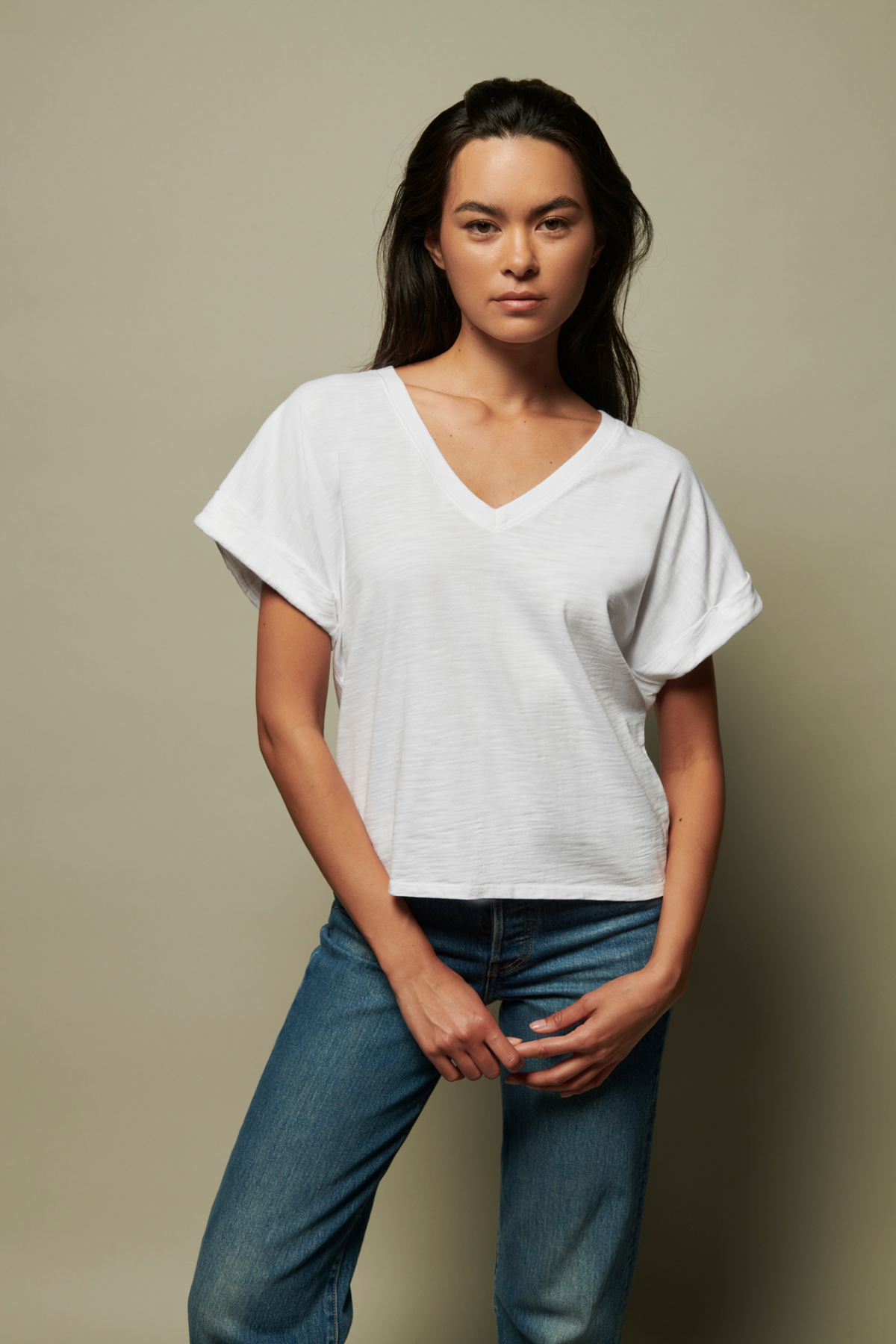 Woman wearing a white t-shirt and blue jeans against a beige background