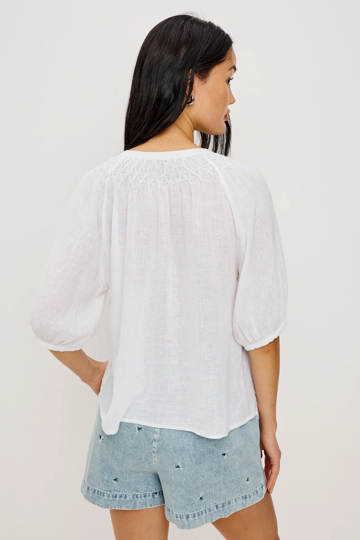 Woman wearing a white blouse and denim shorts on a plain background