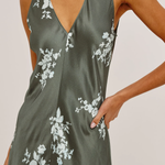 A close-up of a woman wearing a sleeveless satin slip dress in olive green with a white floral print, featuring a deep V-neckline.