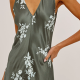 A close-up of a woman wearing a sleeveless satin slip dress in olive green with a white floral print, featuring a deep V-neckline.