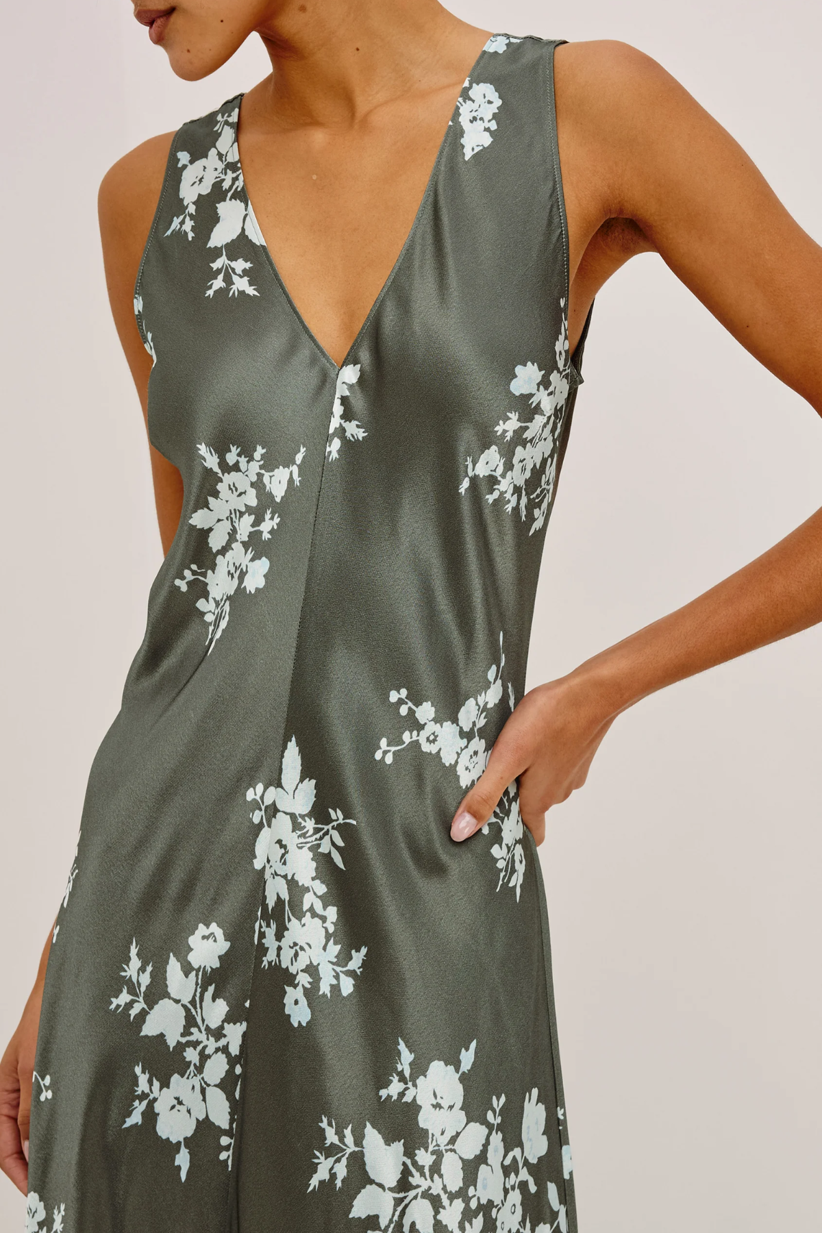 A close-up of a woman wearing a sleeveless satin slip dress in olive green with a white floral print, featuring a deep V-neckline.