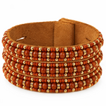 A wide brown suede cuff bracelet decorated with multiple rows of orange-red beads and small gold spacer rings, shown on a plain white background.